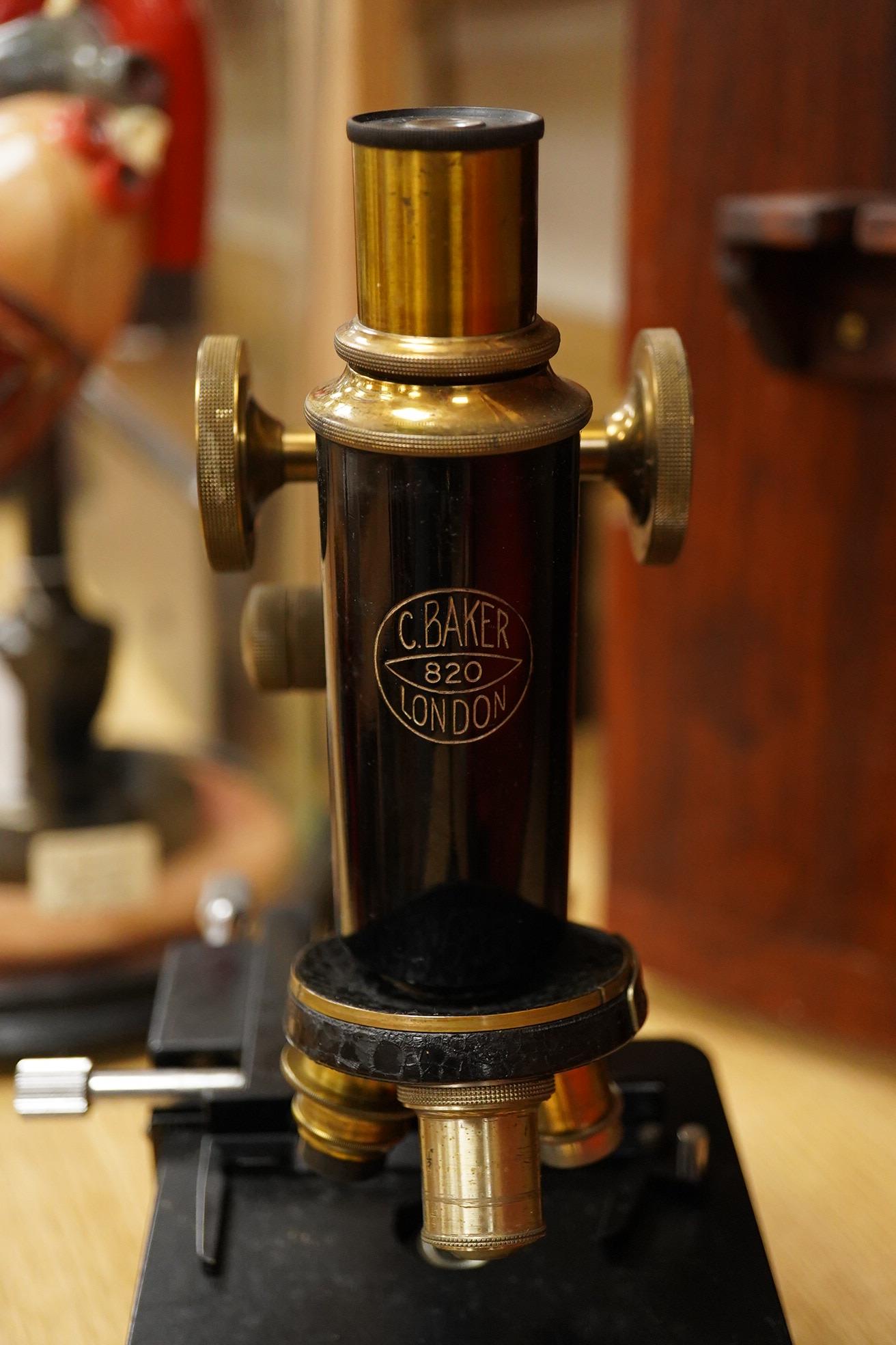 An early 20th century pine and plywood cased microscope by C.Baker, London, containing an integral drawer with alternative lenses, and a magnifying glass on a brass stand, the case dimensions; 38cm high, 18cm wide, 27.5c